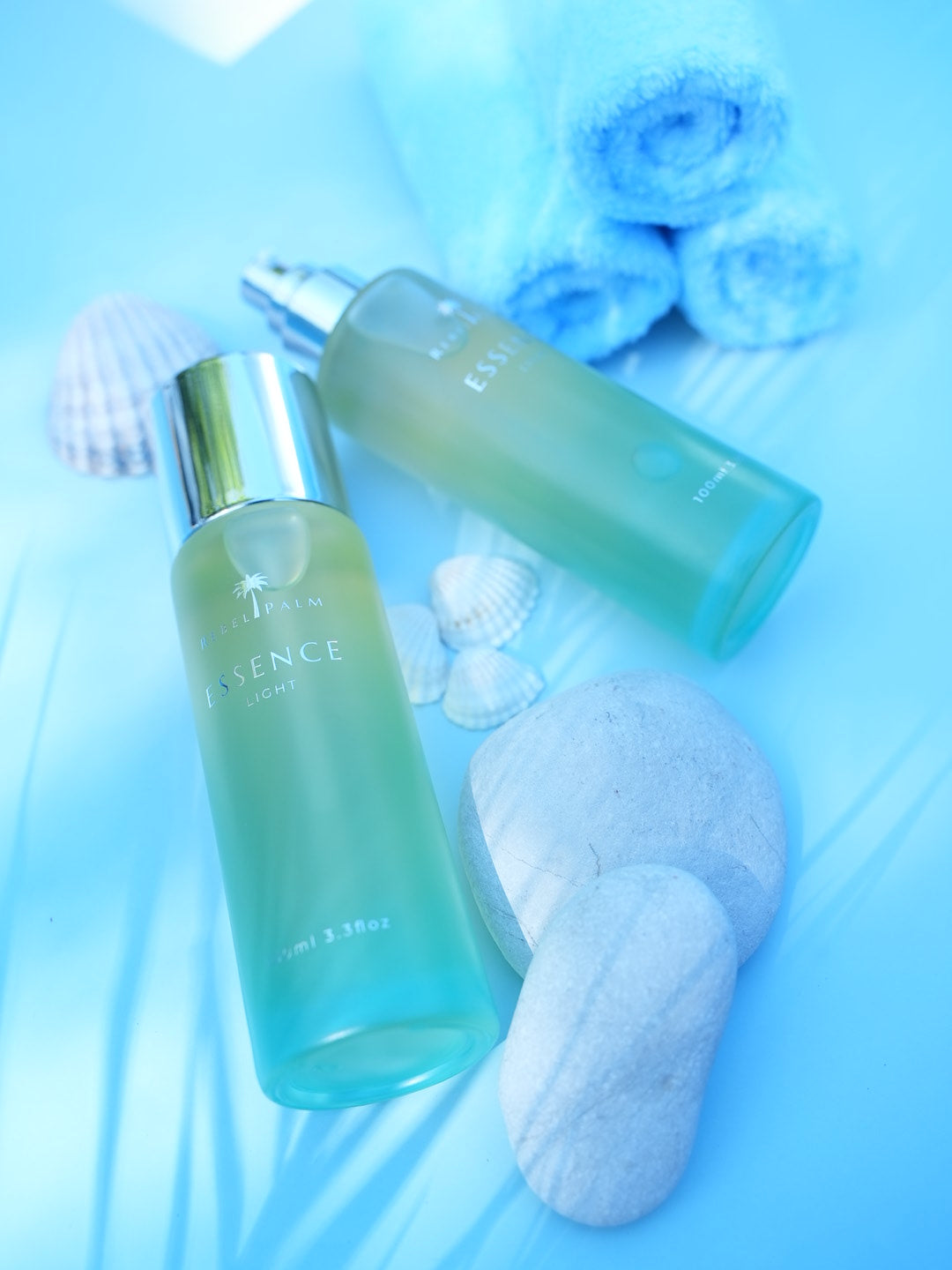 Rebel Palm Essence Light Body Oil 100ml with silver pump cap beside teal gradient glass bottle