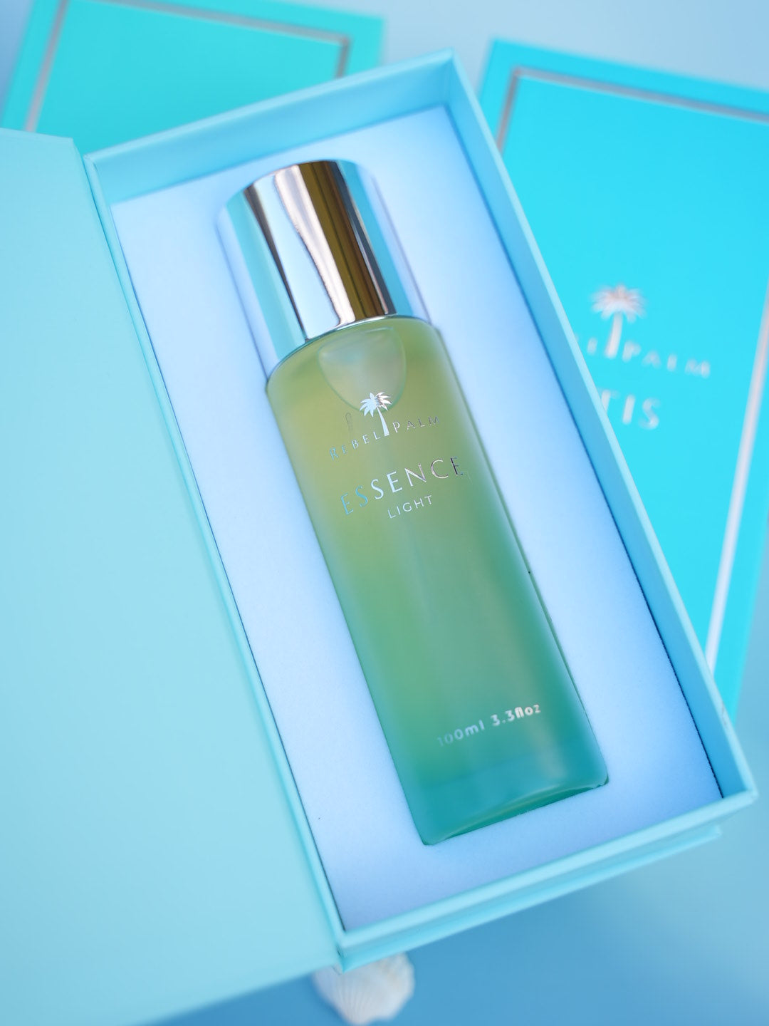 Rebel Palm Essence Light Body Oil nestled in open teal luxury gift box, angled view